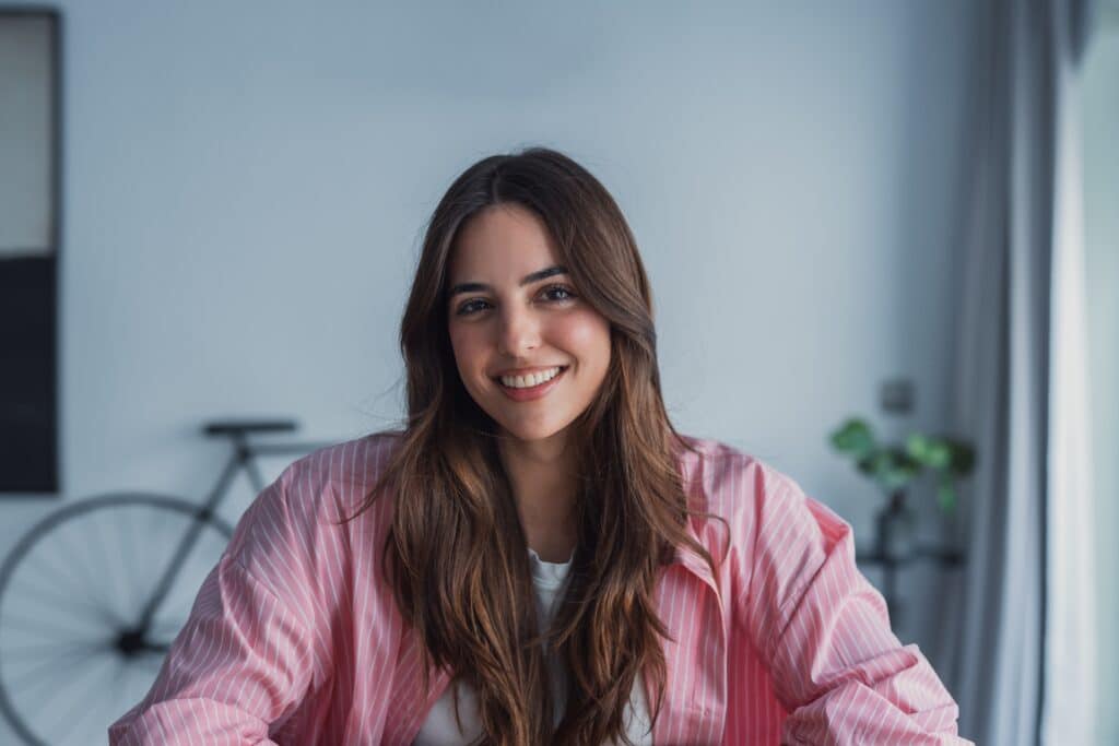 Smiling,Woman,Wearing,A,Pink,Shirt,And,Long,Hair,Sits