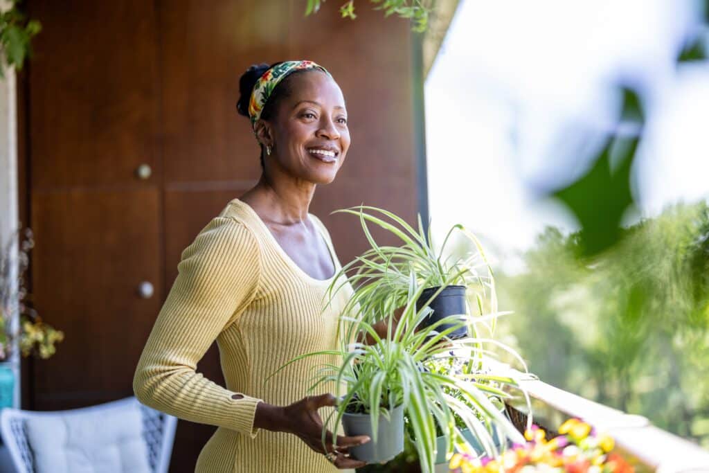 Smiling,Woman,Holding,Potted,Plants,On,The,Balcony,At,Home