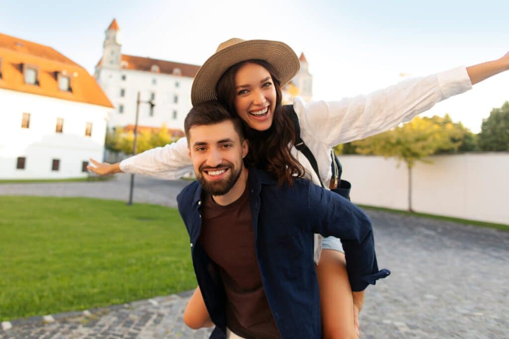Two,Tourists,Happily,Posing,In,Front,Of,Old,Buildings,While